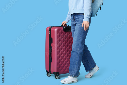 Young woman with backpack and suitcase going somewhere on blue background. Travel concept
