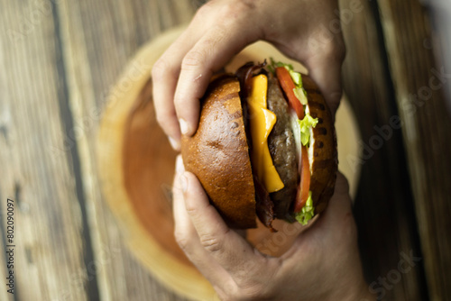Duas mãos segurando um hamburguer em cima de uma mesa de madeira Two hands holding a burger on a wooden table 4