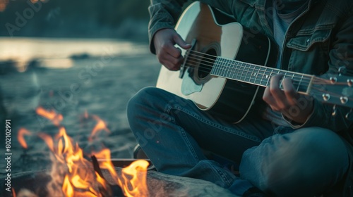 A musician strumming a guitar by a campfire on the beach.