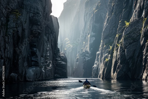 A lone canoeist navigating a narrow river channel between rugged cliffs with dramatic sunlight