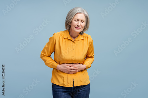 Senior woman holding belly having stomach ache isolated on blue background