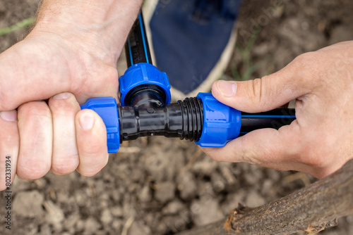 A man installs an automatic drip irrigation system for his garden. Fixing and connecting pipes using a fitting