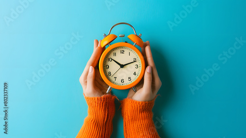 Female hand holding a alarm clock with blue background.