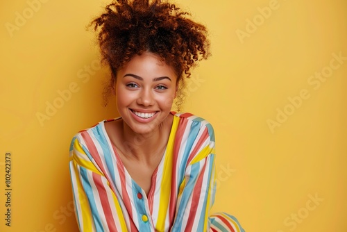Young happy girl in colorful striped pajama on yellow background