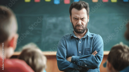 Serious angry male teacher standing with arms crossed in front of classroom exuding authority and sternness. His intense gaze towards pupils highlights moment of discipline