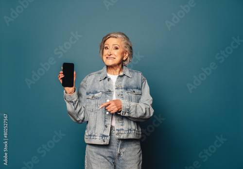 Senior woman recommending mobile app, holding up a smartphone in a studio