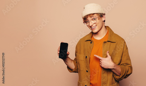 Happy young man recommending a vibrant mobile app with a peach background