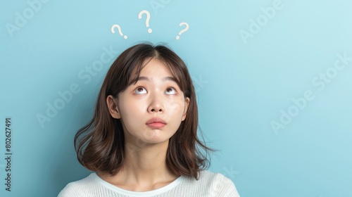 A young woman with a thoughtful expression on her face is looking up at three question marks.