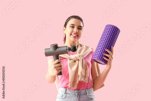Young woman with percussive massager and foam roller on pink background