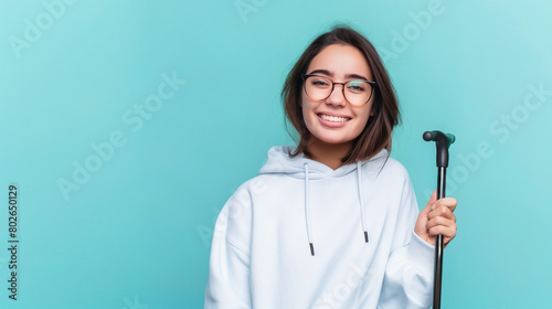 young woman disability advocate holding walking stick, isolated on plain blue color studio background with copy space 
