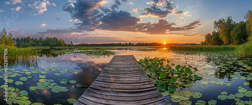 Beautiful summer landscape with a wooden jetty on a lake, sunset sky and lily pads in the foreground, detailed panorama