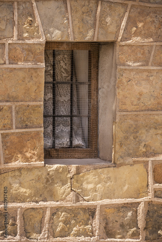 A vintage yellow stone wall with a small window with black bars and wooden frames