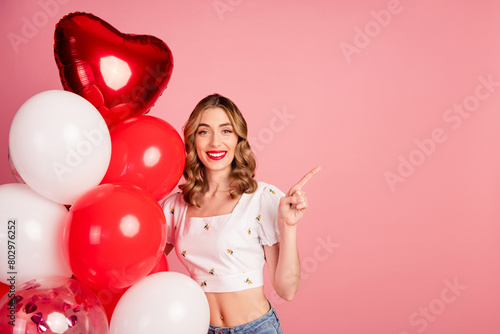 Photo portrait of lovely young woman balloons point empty space dressed stylish white garment hairdo isolated on pink color background