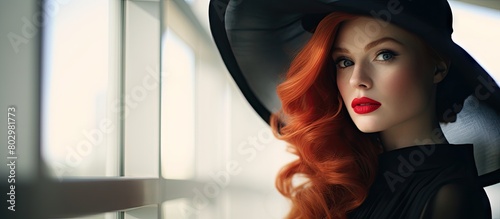 A fashionably dressed redhead girl with bright makeup poses against a large window wearing a red hat and black dress The photo has a toned style reminiscent of Instagram filters Copy space image