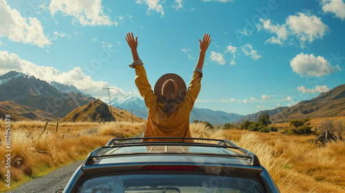 Young happy man waving his arms leaning out of an open car window, set against a backdrop of mountains and the sky. A moment of excitement or joy during a car ride in a scenic outdoor setting. Feeling