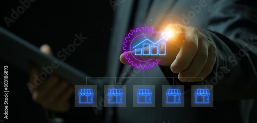 Expanding franchise stores and increasing profitability. Sales growth concept. Businessman working with tablet to show glowing up arrows inside gear and franchise icon on virtual screen.