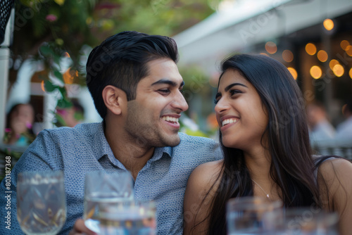 An Indian couple enjoying a restaurant date, laughing together on the terrace. The boyfriend and girlfriend embracing the spring weather while having lunch outdoors.
