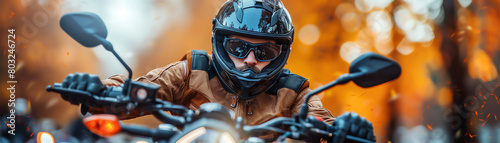 A man in a brown leather jacket and black helmet rides a motorcycle through a fall forest.