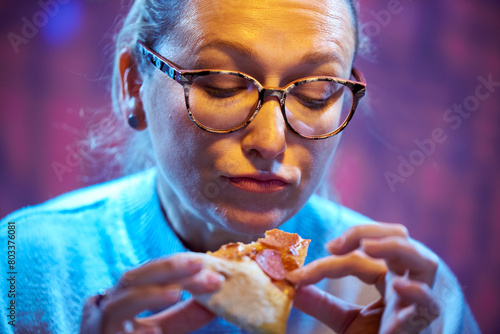 Hungry adult woman in glasses eating pizza with pleasure