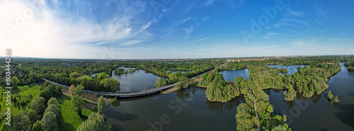 Sunny day aerial view of treelined lake, blue water, white clouds in sky Hanover Ricklinger Teiche Germany