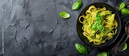 Top-down view of a black bowl filled with tagliatelle pasta, pesto sauce, and basil leaves, along with empty space for text.