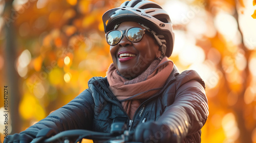 A joyful African American woman wearing a helmet and sunglasses rides a bicycle in an autumn park.
