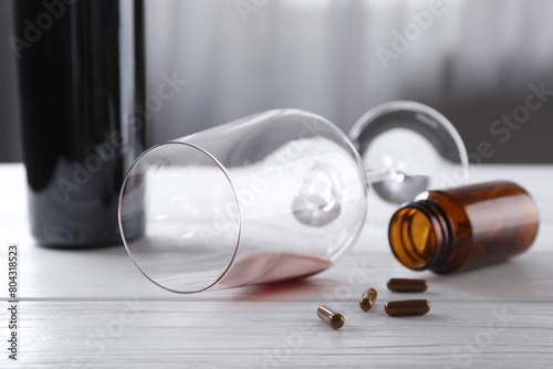 Alcohol and drug addiction. Overturned glass with red wine, bottle and pills on white wooden table, closeup