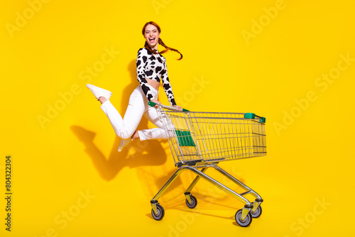 Full length photo of excited cheerful woman wear cow skin print top jumping enjoying shopping isolated yellow color background