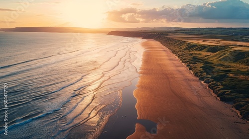 Aerial view of a long, winding coastline bathed in the golden light of a sunset, casting long shadows on the sandy beach