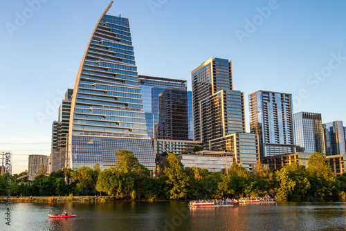 Modern architecture and high-rise buildings of Austin, Texas with summer sunlight reflections on Lady Bird Lake. A ground-level view of the lake and boats on the water.