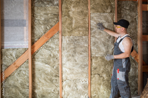 a construction worker insulates the wall of a frame house with mineral wool