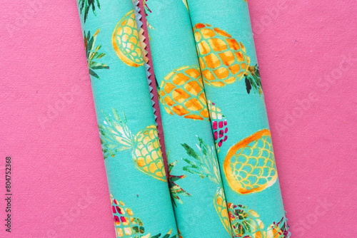 rolled cloth sheets with pineapple prints arranged vertically on pink paper