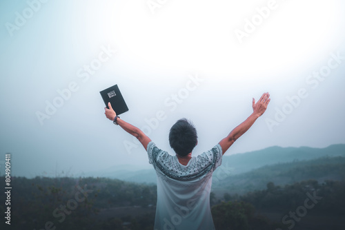 Man raised both hands up and holding bible, pray for blessings to God.