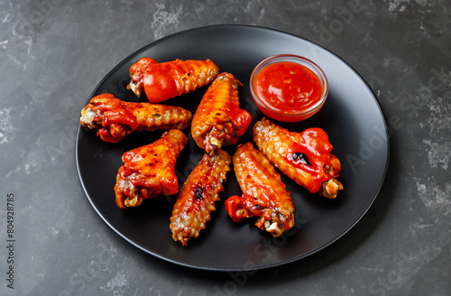 Spicy grilled chicken wings with ketchup on a black plate on a dark slate.