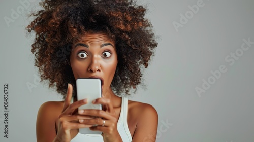 Woman is amazed by content she saw or reads shocking message on mobile phone screen. African American woman opens her mouth in surprise and holds her hand. copy space for text.