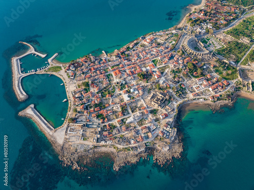 An aerial view of the historic peninsula of Side in Antalya, Turkey. The scene highlights the iconic Apollo Temple, Roman ruins, a charming harbor, and a picturesque townscape.