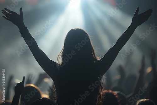The silhouette of a woman raises her arms among a backlit audience, capturing the euphoria and unity of a live music event