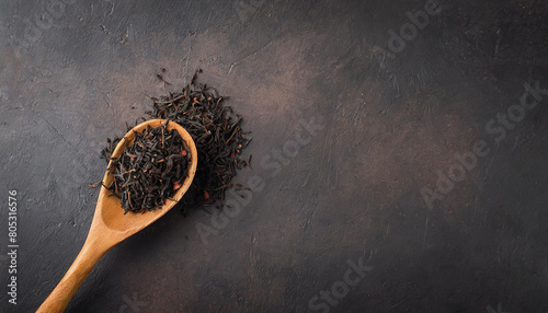 Dry black tea leaves in wooden spoon isolated on a white background, top view.