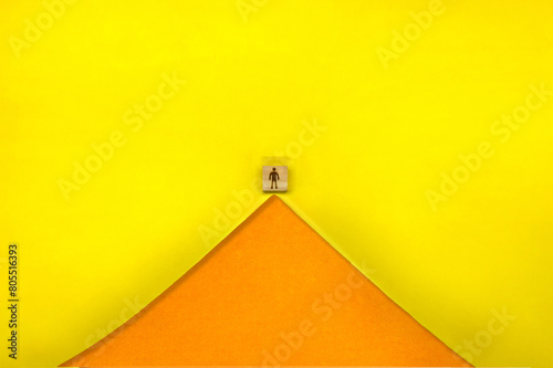 オレンジ色の反り立つ三角形の山の頂上に人のシルエットマークのブロックが立つ黄色い背景