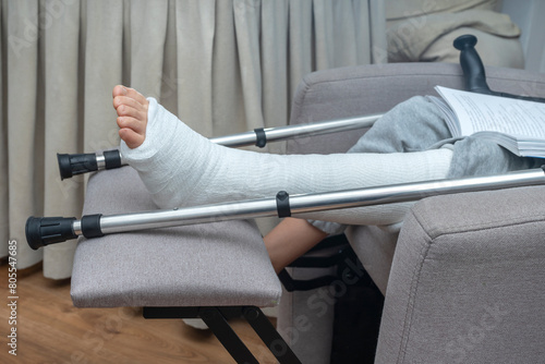 Person with broken leg in a plaster cast with crutches at home. Health care insurance.