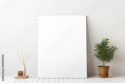 A blank white canvas positioned against a plain white wall in a room, with a potted green plant to the right.