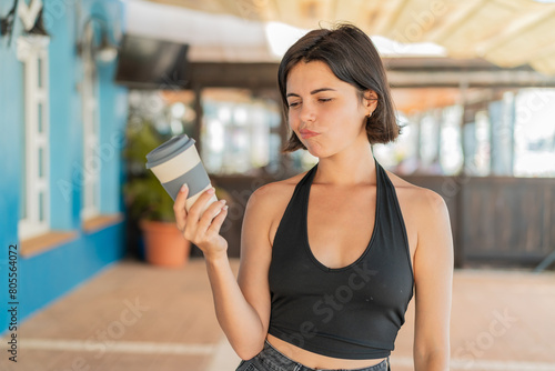 Young pretty Bulgarian woman holding a take away coffee at outdoors with sad expression