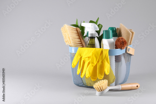 Set of different cleaning supplies in basket on light grey background. Space for text