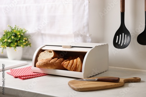 Wooden bread basket with freshly baked loaves on white marble table in kitchen