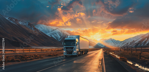 A large semi truck is driving down a road in front of a beautiful mountain range