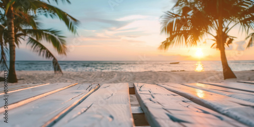 Soft lightning of sunset of a wooden white table at the sandy beach with palms on the background for minimalistic summer idea banner