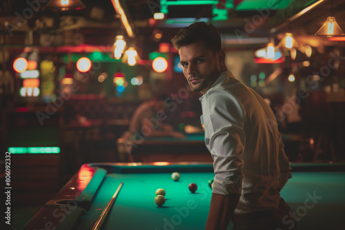 young handsome man with cue opposite to a billiard table playing billiard with friends, in a bar at night out