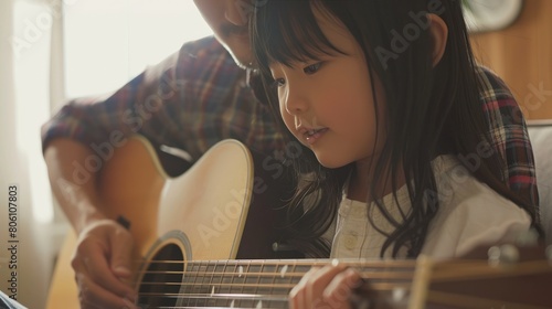 Asian father teaching his daughter to play the guitar in their living room, creating a happy and joyful atmosphere in family.
