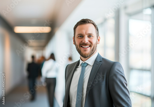 A man in a suit and tie is smiling in a hallway. He is surrounded by other people, some of whom are also wearing suits. Concept of professionalism and formality