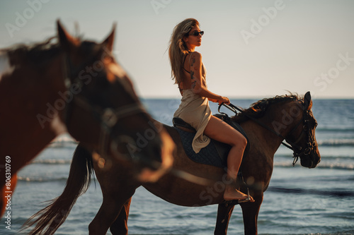 Tattooed beautiful young woman horseback riding on a beach